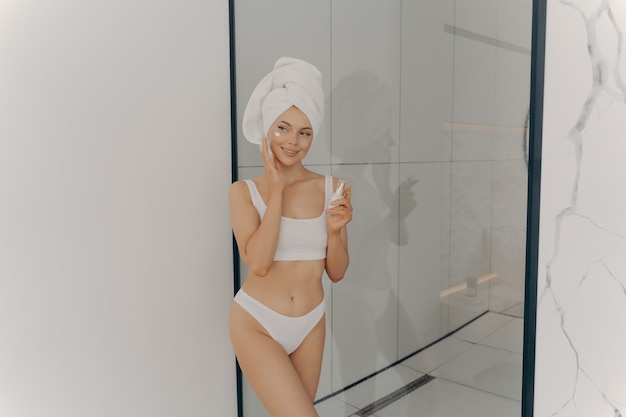 Image of beautiful young girl with towel on head holding moisturizing face cream