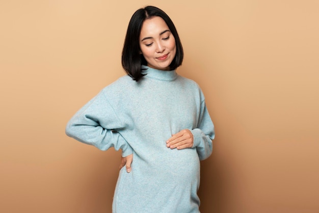 Image of a beautiful young pregnant asian woman posing isolated over beige background