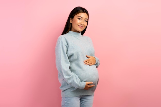 Image of a beautiful young pregnant asian woman posing isolated over pink