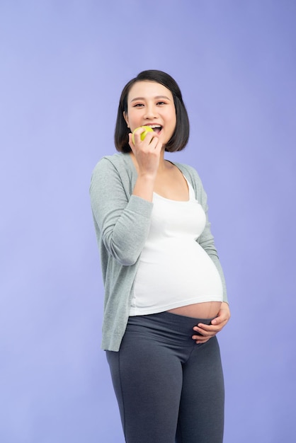 Image of a beautiful young pregnant woman posing isolated over purple wall background holding apple eat healthy food