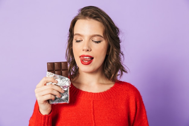 Image of an beautiful young woman posing isolated over purple wall wall holding chocolate.