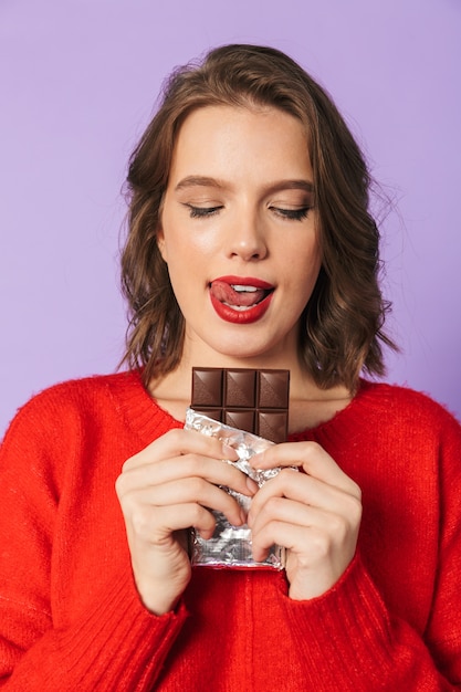 Image of an beautiful young woman posing isolated over purple wall wall holding chocolate.