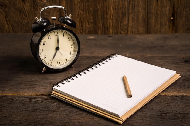 image of a blank notebook and an alarm clock. open and lying flat on wooden for writing message