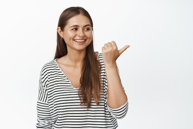 Image of candid happy woman pointing finger and looking right at advertisement smiling and laughing over logo banner white background