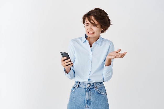 Image of caucasian woman cringe as reading mobile phone screen stare at something disgusting in internet receive awful message white background