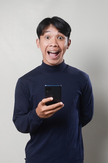 Image of cheerful asian man smiling and using mobile phone