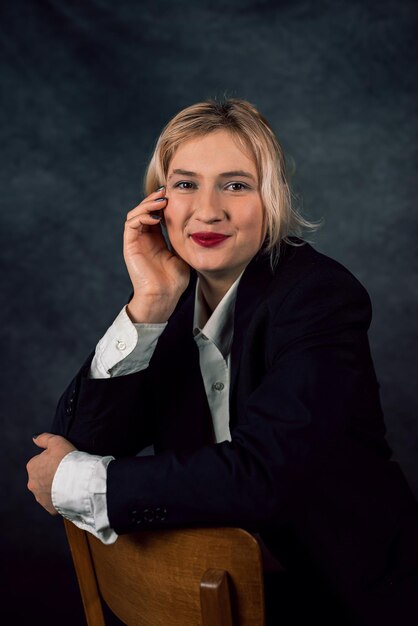 Image of a cheerful office woman with long white hair in business clothes sitting on a chair and looking away