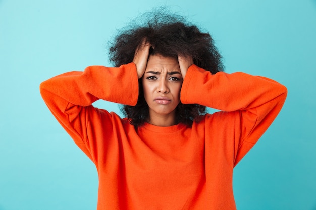 Image closeup of frustrated woman in red shirt looking  and grabbing head with shaggy hair, isolated over blue wall