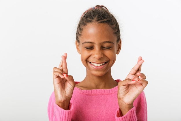 Image closeup of funny african american girl smiling with fingers crossed isolated over white wall