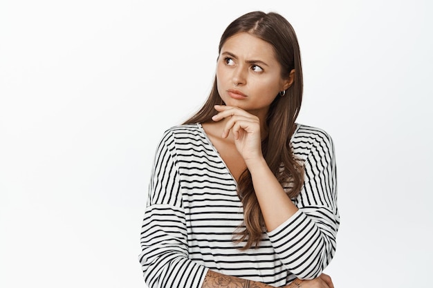 Image of concerned woman thinking, looking at upper left logo with serious, frowned face, white background.