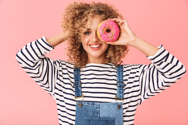 Image of content curly woman 20s wearing casual clothes eating donut while standing