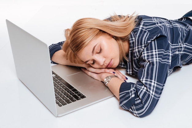 Image of cute young sleeping woman lies near laptop computer isolated on a white background.