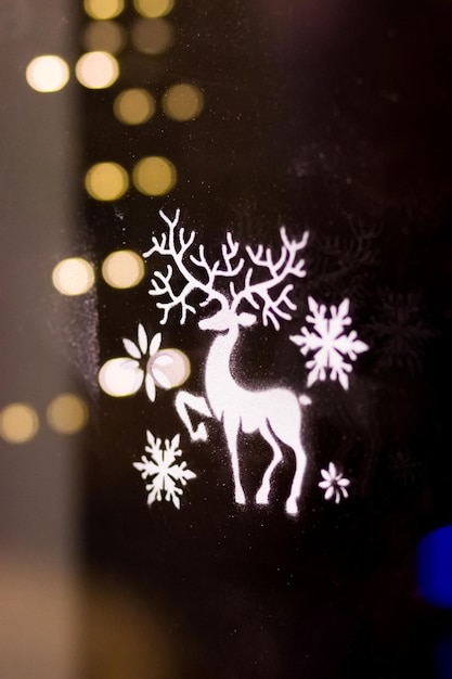 Image of a deer made of artificial snow on a window against a background of garlands Christmas Decoration