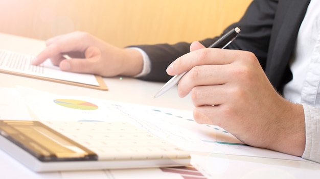 Image of document with charts on background of male and female hands with pens over open notebooks at seminar