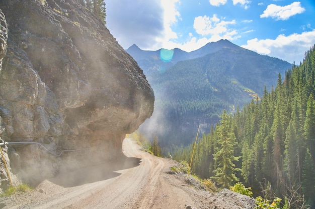 Image of Dusty dirt road dangerously narrow next to cliff edge with overhanging rocks in the mountains