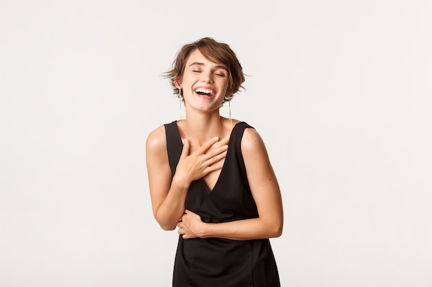 Image of elegant beautiful woman in black dress, laughing ecstatic, standing over white.