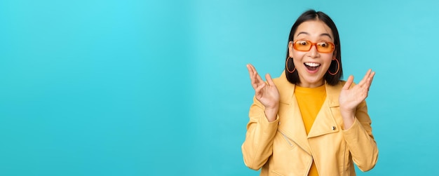 Image of enthusiastic young asian woman celebrating triumphing looking surprised and happy clapping hands satisfied standing over blue background