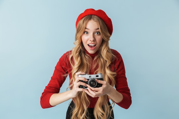 Image of european blond woman 20s wearing red beret holding retro camera isolated 