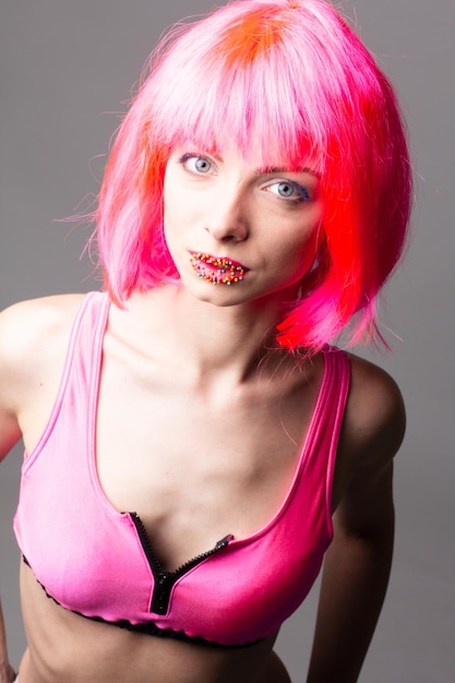 Image of excited beautiful woman in wig laughing while posing with candy isolated over pink background