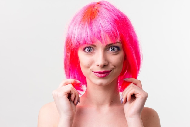 Image of excited beautiful woman in wig laughing while posing with candy isolated over pink background