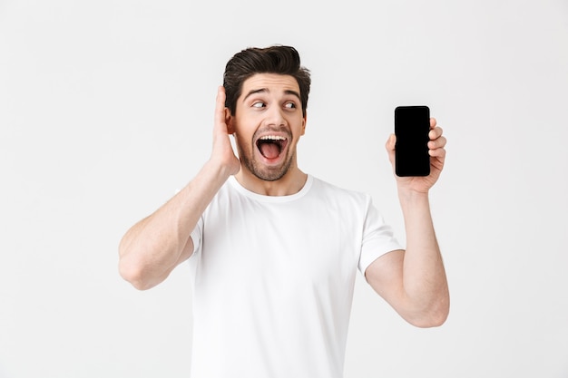 Image of excited happy young man posing isolated over white wall  showing display of mobile phone.