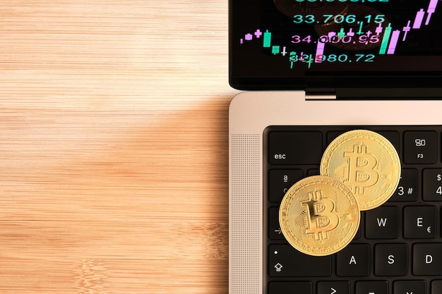 Image from above of bitcoins on laptop keyboard with stock market data on monitor