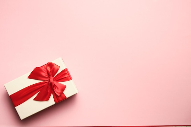 Image from above of a gift with red bow on pink background