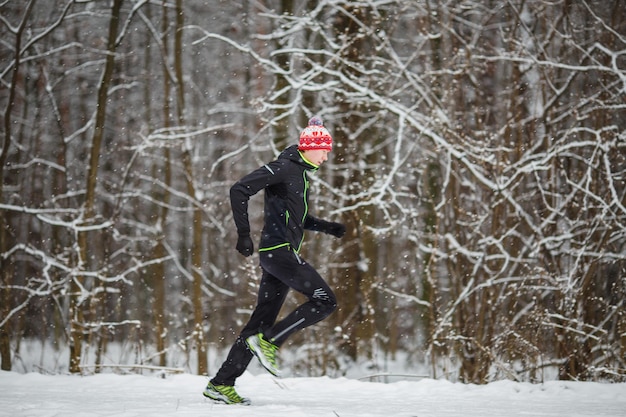 Image from side of man in sportswear red cap on run in winter