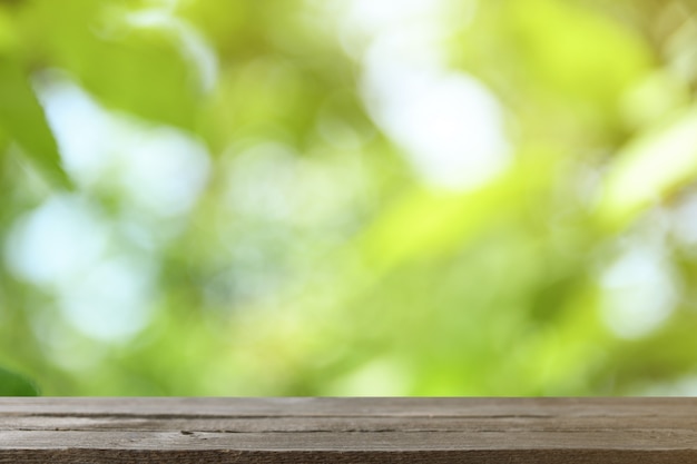 Image of grey wooden table in front of abstract blurred background of trees on a green meadow