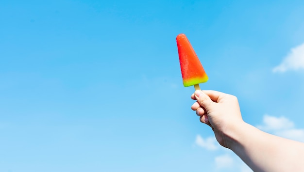 Image of hand holding ice cream on blue sky background