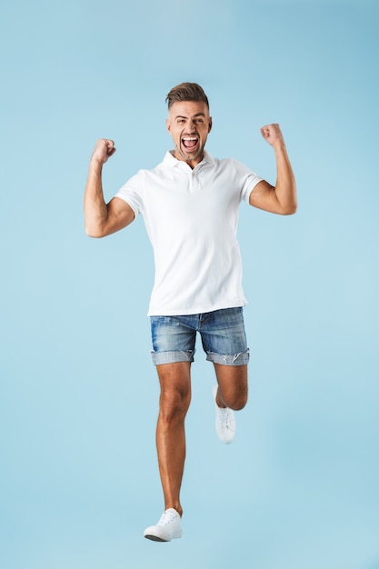 Image of a handsome excited emotional adult man posing over blue wall make winner gesture.