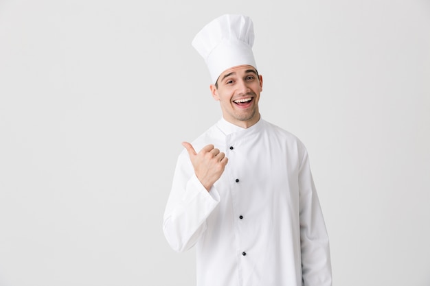 Image of handsome excited young man chef indoors isolated over white wall background pointing.