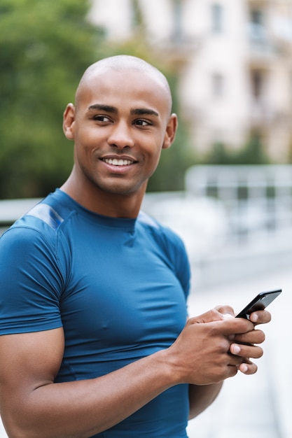 Image of handsome young strong sports man outdoors using mobile phone chatting.