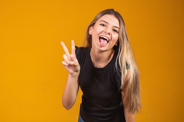 Image of happy young man standing isolated over yellow background showing peace gesture. Camera looking.