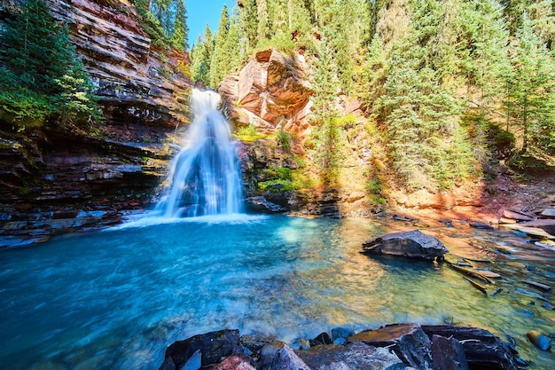 Image of Hidden waterfall with bright blue water in gorge with pine trees