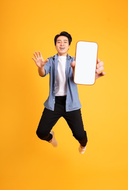 Image of jumping up asian man holding smartphone in hand isolated on yellow background