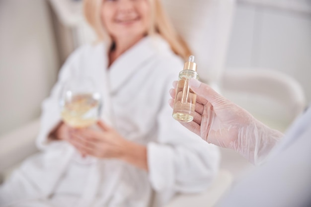 Image of little bootle with skin face serum in cosmetologist hand