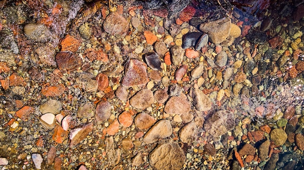 Image of Looking down at shallow riverbed with round colorful rocks