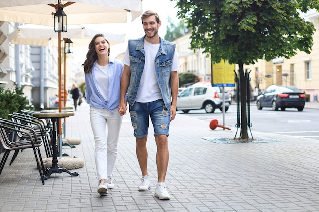 Image of lovely happy couple in summer clothes smiling and holding hands together while walking through city street.