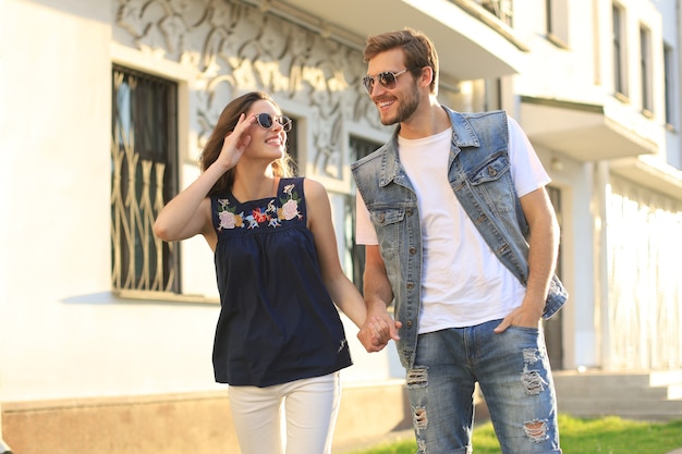 Image of lovely happy couple in summer clothes smiling and holding hands together while walking through city street.