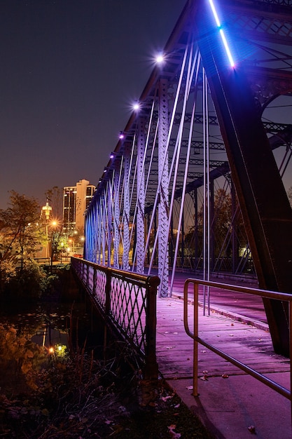 Image of Metal bridge leading into a town is lit up purple at night