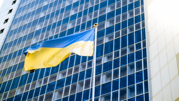 Image of national flag of Ukraine against modern office building. Concept of Ukrainian economics, development and politics