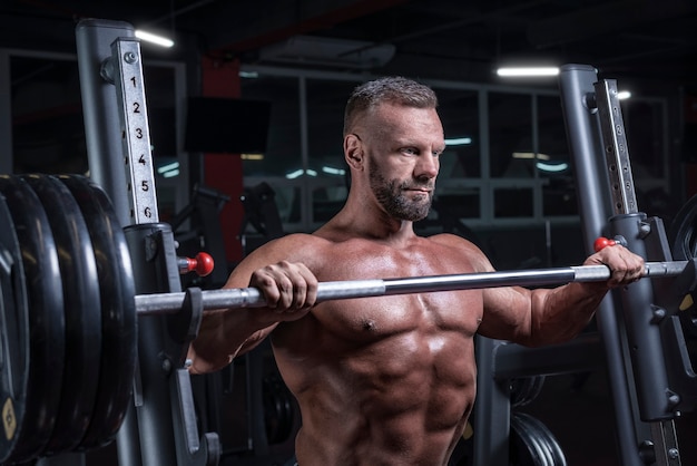 Image of a powerful athlete standing near a barbell rack in a gym. Fitness and bodybuilding concept. Mixed media