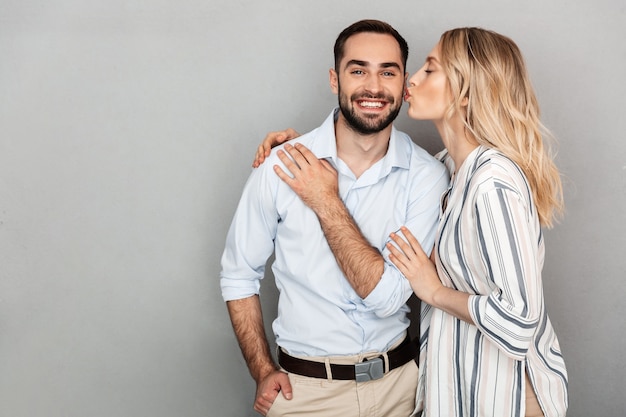 Image of pretty couple in casual clothing smiling while woman kissing handsome man isolated