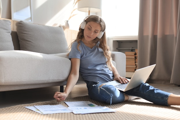 Image of pretty woman working with laptop while sitting on floor at home.