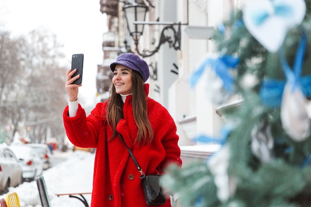 Image of a pretty young woman outdoors walking at snow winter street take selfie by mobile phone.