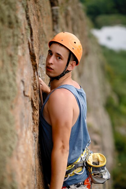 Image of rock climber in helmet climbing up mountain on wall of picturesque landscape.