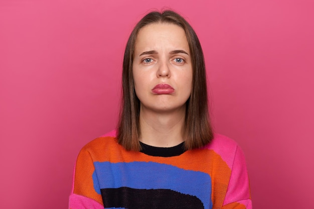 Image of sad depressed stressed woman wearing colorful jumper posing isolated over pink background looking at camera with pout lips being in bad mood expressing negative emotions