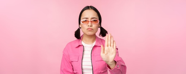 Image of serious stylish asian girl in sunglasses showing stop prohibit gesture taboo sign saying no