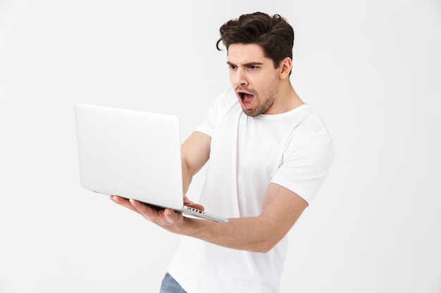 Image of shocked confused young man posing isolated over white wall using laptop computer.